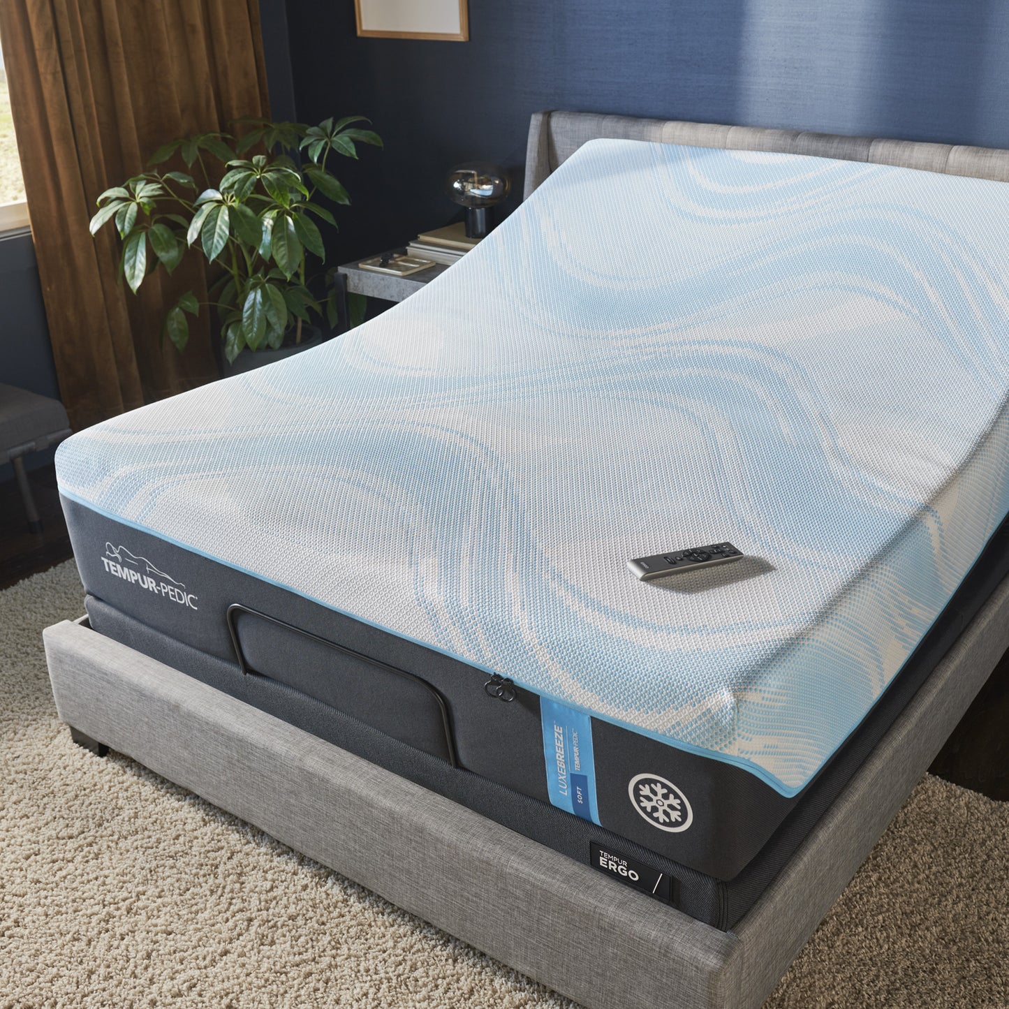 TEMPUR-Ergo adjustable base shown with a Tempur-Pedic cooling mattress in an elevated head position, placed in a modern bedroom with remote control on the bed.