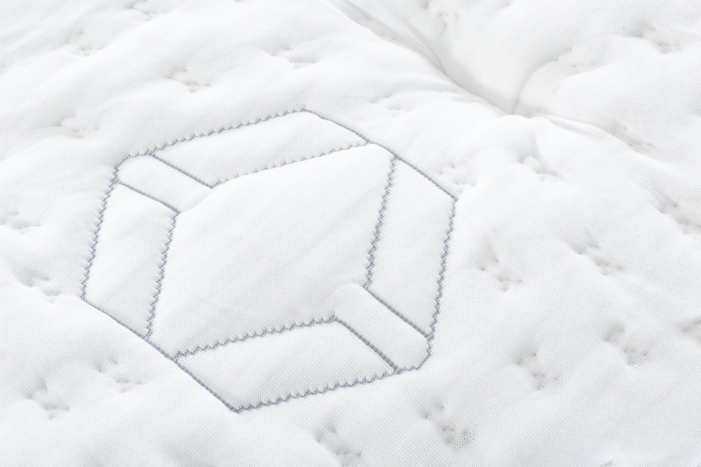Close-up of a white quilt with hexagonal pattern and blue stitching